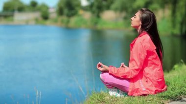 Spor kıyafetli kız göletin kenarında oturup meditasyon yapıyor. Güzel bir kadın göl kenarında meditasyon yapıyor. Meditasyon - bireyin zihni çalıştırdığı, eğittiği ya da bir bilinç biçimini tetiklediği uygulama