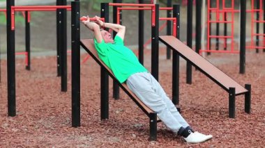 Kıdemli adam karın kaslarını şişiriyor ve kalorileri yakıyor. Aktif, gri saçlı, yeşil tişörtlü sporcu spor sahasında fiziksel egzersiz yapıyor açık hava spor salonunda antrenman yapıyor.