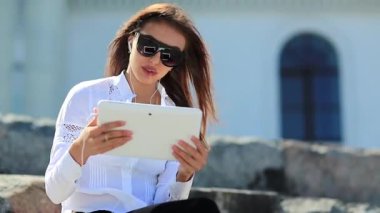İş kadını tablet bilgisayarla iletişim kuruyor. Beyaz tabletli gözlüklü çekici bir kadın Skype üzerinden iletişim kuruyor, neşeli bir ruh hali içinde.