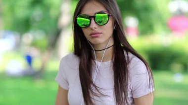 Yeşil güneş gözlüklü, kulaklıklı güzel bir kız kameraya bakıyor. Gözlüklü ve kulaklıklı güzel bir kadın müzik dinliyor.