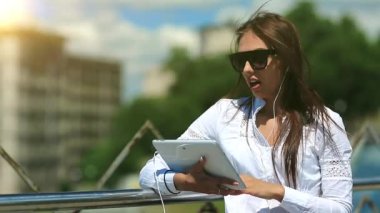 Elinde tablet bilgisayarla güneş gözlüklü çekici bir kız Skype üzerinden iletişim kuruyor. İş kadını tablet bilgisayarla iletişim kuruyor