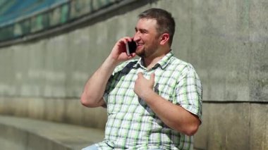 İş adamı akıllı telefon aracılığıyla iletişim kurar. Adam cep telefonuyla konuşuyor ve el kol hareketi yapıyor. Kırmızı cep telefonlu şişman komik adam. Elinde kırmızı cep telefonu olan, kareli tişörtlü, mutlu, sosyal bir adam.