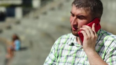 Adam cep telefonuyla konuşuyor. İş adamı akıllı telefon aracılığıyla iletişim kurar. Kırmızı cep telefonlu, kareli gömlekli, şişman, sosyal bir adam.