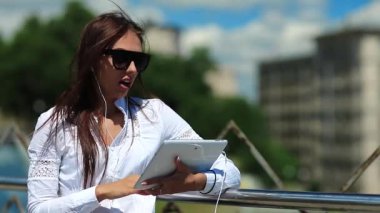 Elinde tablet bilgisayarla güneş gözlüklü çekici bir kız Skype ya da görüntülü sohbet yoluyla iletişim kuruyor. İş kadını tablet bilgisayarla iletişim kuruyor