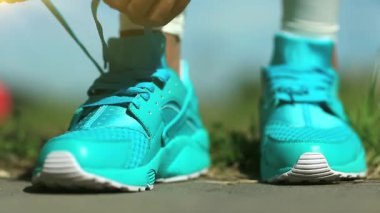 Sporcu kadın koşu ayakkabılarını bağlıyor. Runner uzun mesafe koşmaya hazırlanıyor. Kız spor için gidiyor, mavi spor ayakkabılar yakın plan.