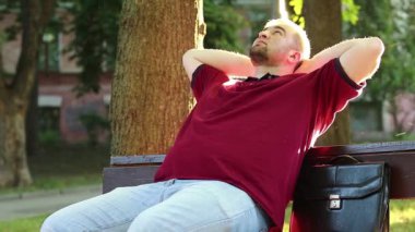 İş adamı şehir parkında bankta oturur ve dinlenir. İnsan sıkı çalışma gününden sonra rahatlar.