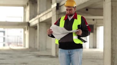 Proje alanında inşaat belgesi olan bir işçi. İnşaat alanında tasarım çizimleri olan sert şapkalı ana mimar.
