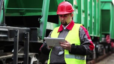 Trenin yanında tablet bilgisayarı olan bir demiryolu çalışanı. Tren istasyonundaki tren trafiği müfettişi tablet bilgisayarına not alır.
