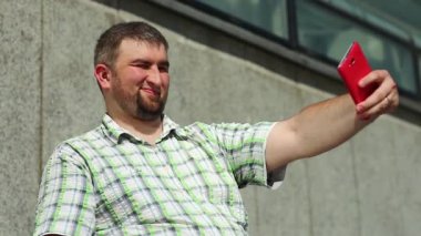 Şişko komik adam kırmızı akıllı telefondan selfie çekiyor. Adam cep telefonuyla fotoğraf çekiyor.