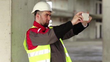 Proje alanında akıllı telefonu olan beyaz şapkalı bir inşaat işçisi. İnşaat alanındaki işçiler akıllı telefondaki videoları kaydediyor