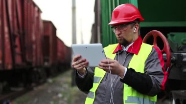 Demiryolu işçisi, yük trenleri arasında tablet bilgisayarla konuşur. Yük istasyonundaki demiryolu işçisi tablet bilgisayarla görüntülü sohbet yoluyla konuşuyor