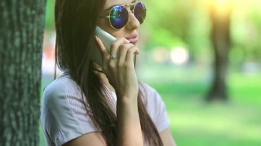 Şehir parkında güzel bir kadın ağacın yanında duruyor ve akıllı telefondan konuşuyor. Doğasında akıllı telefon olan bir iş kadını. Çekici kız cep telefonuyla konuşur, arka planda yanıp sönen güneş...