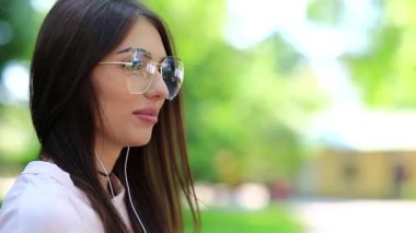 Akıllı telefonlu güzel bir kadın müzik dinler. Gözlüklü, akıllı telefon ve kulaklıklı çekici bir kadın halk bahçesinde müzik dinliyor.