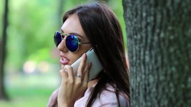 Uzun saçlı güzel kadın ağacın yanında duruyor ve cep telefonuyla konuşuyor. Çekici kız cep telefonuyla konuşuyor. Doğada akıllı telefonu olan bir iş kadını.