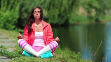 Güzel bir kadın göl kenarında meditasyon yapıyor. Spor kıyafetli kız göletin kenarında oturup meditasyon yapıyor. Meditasyon - bireyin zihni çalıştırdığı, eğittiği ya da bir bilinç biçimini tetiklediği uygulama