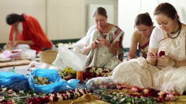 UKRAINE, KIEV, 4 AĞUSTOS 2017: Hindu geleneksel renkli kostümlü kadınlar Krishna tapınağında çiçek çelengi yapıyorlar, Krishna tanrısına hizmet ediyorlar