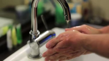 Adam ellerini sabunla yıkıyor. Adam ellerini lavaboda yıkıyor.