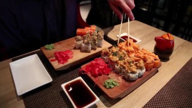 Adam Japon restoranında suşi yiyor. Masada Japon yemeği var. Adam restoranda masada oturur ve Japon yemeği yer.