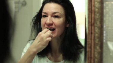 Ağız temizliği. Diş fırçalı kız. Kadın aynaya bakar ve banyoda dişlerini fırçalar. Banyoda diş fırçasıyla dişlerini fırçalayan bir kız.