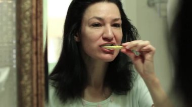 Kadın aynaya bakar ve banyoda dişlerini fırçalar. Banyoda diş fırçasıyla dişlerini fırçalayan bir kız. Ağız temizliği. Diş fırçası olan kız.