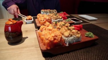 Masada Japon yemeği var. Adam Japon restoranında suşi yiyor. Adam restoranda masada oturur ve Japon yemeği yer.