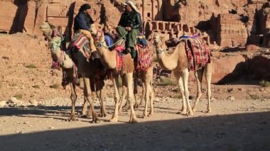 JORDAN, PETRA, 5 Aralık 2016: Ürdünlüler, başlangıçta Ürdün 'ün tarihi ve arkeolojik kenti olan Raqmu olarak bilinen Petra' daki Kraliyet Mezarları yakınlarındaki develer üzerinde. Arka planda İpek ve Vazo Mezarları