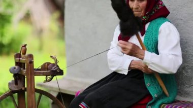 Yaşlı kadın bankta oturuyor ve dönen tekerlekle distaff ile çalışıyor. Ukraynalı yaşlı kadın evinin yanındaki bankta oturur ve iplik örer. Dönen tekerli bir kadın, el işi.