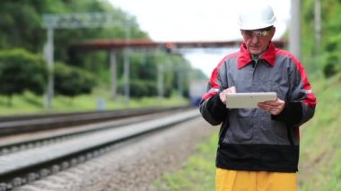Demiryolu çalışanı ve tablet bilgisayarı demiryolu hattında. Demiryolu trafiği müfettişi tablet bilgisayarına not alır. Elinde tabletle demiryolu işçisi trene bakıyor.