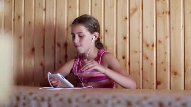 Akıllı telefonlu bir kız masada oturur, müzik dinler ve şarkı söyler. Beyaz akıllı telefonu ve kulaklığı olan kız müzik dinler, el kol hareketi yapar ve şarkı söyler.