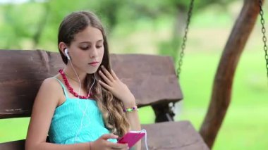 Akıllı telefonlu çekici bir kız bankta oturuyor. Mavi elbiseli kız oyunu onun akıllı telefonuyla oynuyor. Güzel kız salıncakta oturuyor ve onun kırmızı akıllı telefonunu kullanıyor. Akıllı telefonu olan bir kadın.