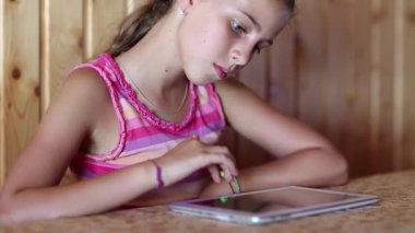 Kız masada oturuyor ve tablet bilgisayar kullanıyor. Güzel kız tablet kullanıyor. Kadın oyunu tablet bilgisayarında oynuyor.