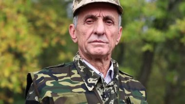 Askeri üniformalı adam kameraya bakıyor. Ormanda askeri üniformalı emekli subay.