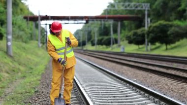 Sarı üniformalı tamirci elinde kürekle demiryolu hattını tamir ediyor. Sarı üniformalı demiryolu işçisi elinde kürekle tren yolunu tamir ediyor. Demiryolunda küreği olan bir işçi.