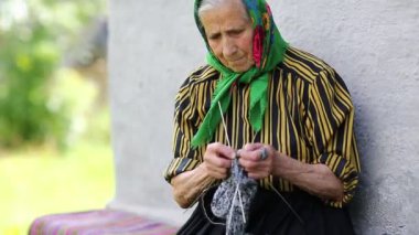 Ukraynalı yaşlı kadın örgü örüyor. Yaşlı kadın bankta oturup yün çoraplar örüyor. Yeşil başörtülü yaşlı kadın evinin yanında oturup çorap örüyor. Eşarplı kadın yün çorap örüyor.