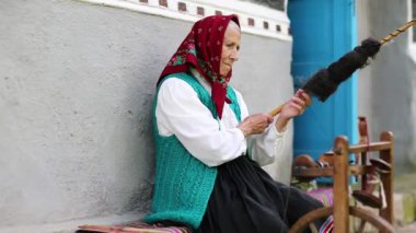 Yaşlı kadın bankta oturuyor ve dönen tekerlekle distaff ile çalışıyor. Ukraynalı yaşlı kadın evinin yanındaki bankta oturur ve iplik örer. Dönen tekerli bir kadın, el işi.