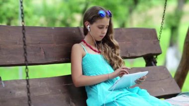Çekici kız salıncakta oturuyor ve tablet bilgisayarı tutuyor. Tablet bilgisayarında oyun oynayan bir kız. Tabletli güzel kız bahçede bankta oturuyor. Tabletli güzel kız.