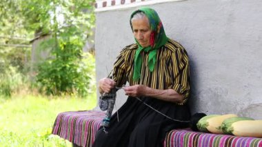 Ukraynalı yaşlı kadın örgü örüyor. Yaşlı kadın bankta oturup yün çoraplar örüyor. Yeşil başörtülü yaşlı kadın evinin yanında oturup çorap örüyor. Eşarplı kadın yün çorap örüyor.