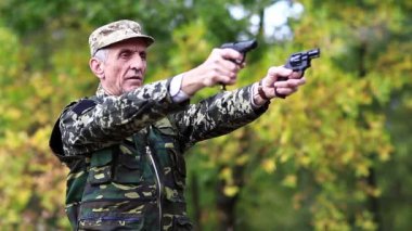 Askeri üniformalı bir asker iki havalı tabancayla ateş eder. Yaşlı adam ormanda iki tabanca ateşler. Üniformalı asker tabancayla ateş ediyor. Poligondaki emekli memur. Sesli video