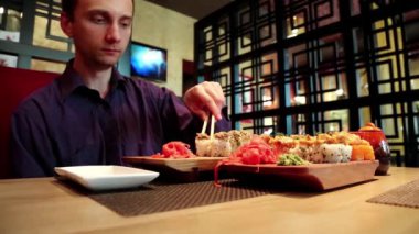 Adam Japon restoranında suşi yiyor. Adam restoranda masada oturur ve Japon yemeği yer.