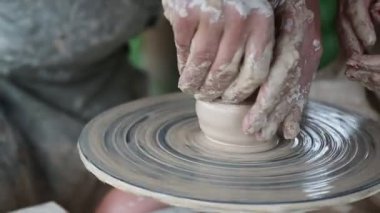 Kadın ve erkek çömlek çarkında demlik yapıyorlar. Bir çömlekçinin elleri ve çırağı. Kadın çömlekçinin öğrencisidir. Erkek ve kadın elleri yakın.