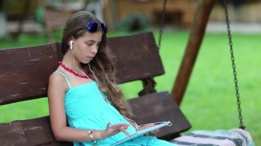 Güzel kız salıncakta oturur ve tablet bilgisayar kullanır. Güzel kız bahçede bankta oturuyor ve el bilgisayarını tutuyor. Tablet bilgisayarda oyun oynayan kız. Tabletli güzel kız.