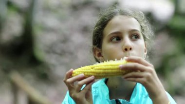 Mavi ceketli güzel kız mısır yiyor ve etrafına bakıyor. Kız sarı mısır yiyor. Mısır koçanı olan bir kadın.