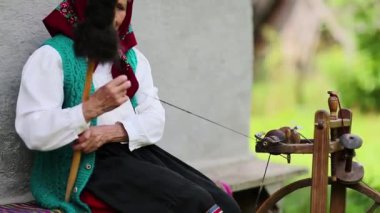 Yaşlı kadın bankta oturur ve dönen tekerlekle distaff üzerinde çalışır. Ukraynalı yaşlı kadın evinin yanındaki bankta oturur ve iplik örer. Dönen tekerli bir kadın, el işi.