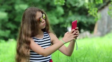 Uzun saçlı güzel bir kız akıllı telefonunda selfie çekiyor. Gözlüklü çekici kız telefonunda selfie çekiyor. Kırmızı cep telefonlu güzel bir kız fotoğraf çekiyor. Kadın akıllı telefondan fotoğraf çekiyor.