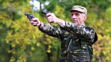 Askeri üniformalı bir asker tabancayla ateş ediyor. Poligondaki emekli memur. Askeri üniformalı bir asker iki havalı tabancayla ateş eder. Yaşlı adam ormanda iki tabanca ateşledi.
