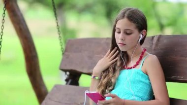 Akıllı telefonlu çekici bir kız bankta oturuyor. Mavi elbiseli kız oyunu onun akıllı telefonuyla oynuyor. Güzel kız salıncakta oturuyor ve onun kırmızı akıllı telefonunu kullanıyor. Akıllı telefonu olan bir kadın.