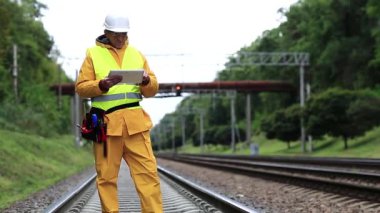 Demiryolu trafiği müfettişi tablet bilgisayarına not alır. Demiryolu çalışanı sarı üniformalı demiryolu hattında. Sarı üniformalı ve elinde tablet bilgisayar olan beyaz şapkalı demiryolu işçisi.
