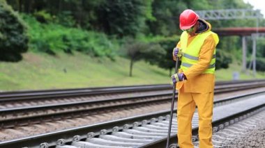 Sarı üniformalı demiryolu işçisi elinde levyeyle demiryolu hattını onarıyor. Sarı üniformalı demiryolu işçisi elinde levyeyle demiryolunu tamir ediyor. Demiryolunda metal levyesi olan bir işçi.