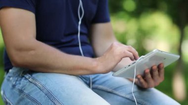 Adam tablet bilgisayarındaki fotoğraflara bakıyor. Beyaz tablet tabletli ve kulaklıklı erkek ellerini kapat. Adam beyaz tablet tableti tutuyor. Adam tablet bilgisayarındaki fotoğraflara bakar ve bakar.