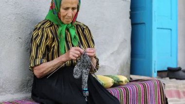 Ukraynalı yaşlı kadın örgü örüyor. Yaşlı kadın bankta oturup yün çoraplar örüyor. Yeşil başörtülü yaşlı kadın evinin yanında oturup çorap örüyor. Eşarplı kadın yün çorap örüyor.